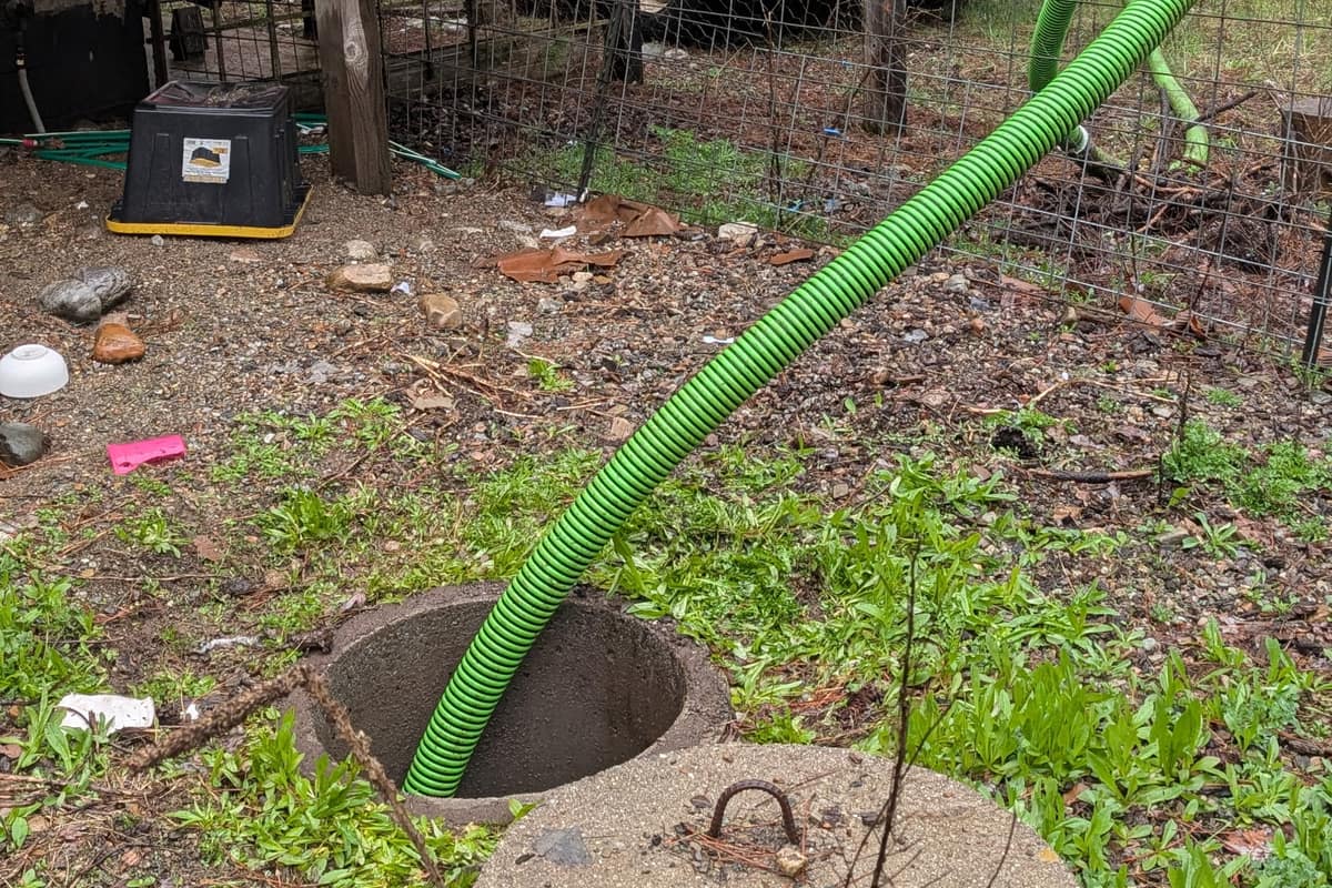 Suction hose running into an open septic tank, lid exposed at grade